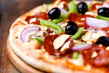 Pizza with chorizo ​​sausage, mozzarella cheese, green pepper and black olives. Rustic wooden background. Soft focus.	