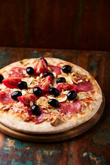 Pizza with salami, tomatoes and mozzarella cheese and black olives. Rustic wooden background. Soft focus. Close up.