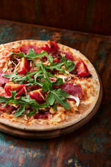 Pizza with ham, salami, tomatoes and mozzarella cheese. Rustic wooden background. Soft focus. Close up.	
