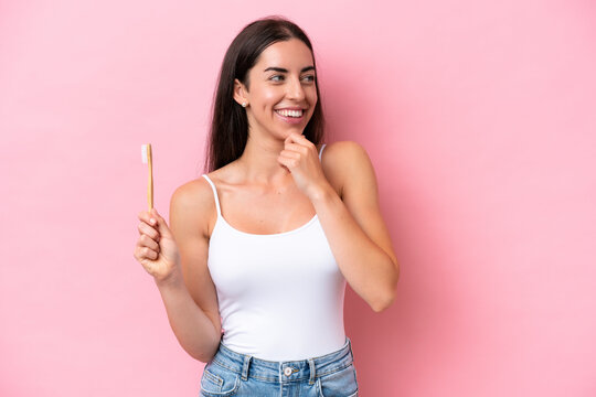 Young caucasian woman brushing teeth isolated on pink background thinking an idea and looking side - Powered by Adobe