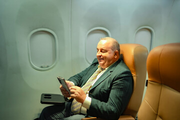 Heavy set Caucasian businessman enjoying airplane journey, smartphone in hand at window seat. Great for airline service ads, aviation lifestyle, global tourism, and modern passenger travel experience.