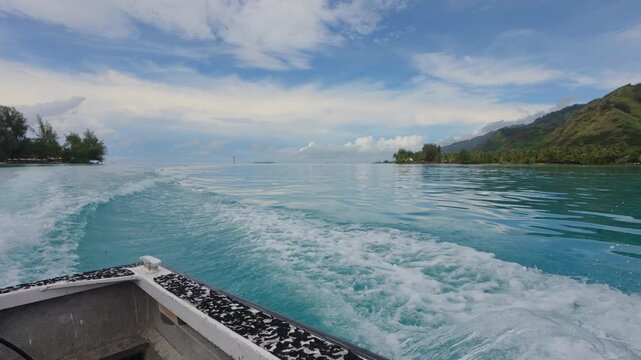 View from a boat leaving a turquoise lagoon, with mountains and palm trees under a blue sky