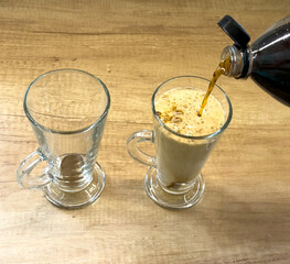 Instant coffee mixed with cold cola in a glass mug on wooden table, refreshing iced coffee drink...
