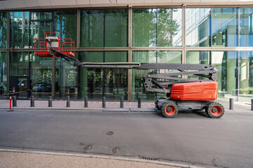 Red articulated boom lift parked on a city street in front of a modern glass building © Jarama