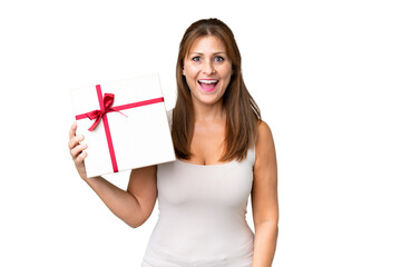 Middle age caucasian woman holding a gift over isolated background with surprise and shocked facial...