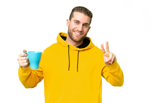 Young handsome blonde man holding cup of coffee over isolated background smiling and showing victory sign