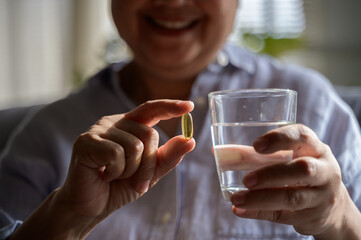 Close up hand of an elderly Asian woman is pouring vitamins from a bottle to take for boosting her...