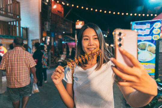 Happy traveler asian woman use mobile phone selfie with grilled crab skewer on hand in Chiang Khan Walking Street night market in Loei Thailand Lifestyle travel concept