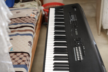 A piano keyboard near a bed in a small room set up