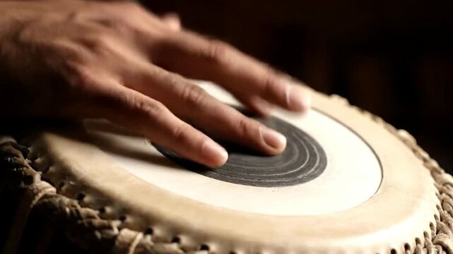 A musician's hand gracefully playing a traditional Indian tabla drum in a close-up shot.