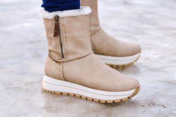 Fashionable suede boots on icy frozen street closeup with ice sidewalk in winter weather showing...