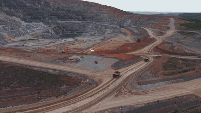 Aerial view of open pit mine with heavy machinery and haul trucks on winding road in quarry gold, copper and iron ore.