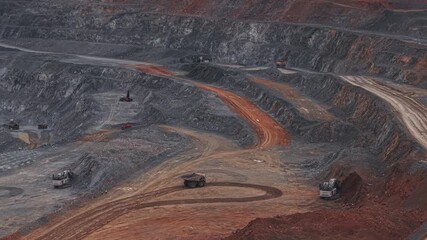 Open pit mine with heavy machinery and haul trucks on winding road in quarry gold, copper and iron ore. Aerial view mining industry.