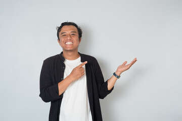 Asian man smiling and pointing sideways, showing cheerful and confident expression. Concept of direction, presenting, introducing, and positive communication on white background.