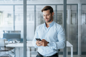 Smiling European or Latin hispanic businessman holding smartphone in office. Middle aged male man manager using cell phone mobile app. Digital technology and solutions for business concept. Copy space