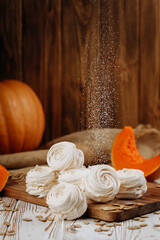 Pumpkin marshmallow sweets with powdered sugar falling, rustic autumn wooden background