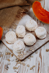 Autumn pumpkin marshmallows on rustic wooden background with seeds and burlap