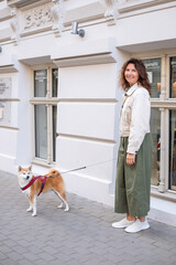 Shiba Inu dog on leash stands beside smiling woman in stylish outfit, enjoying a beautiful morning walk, showcasing companionship and joy in vibrant urban setting