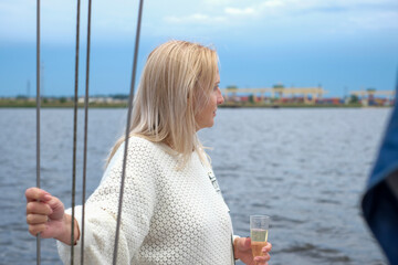 Fototapeta premium Woman with blonde hair, enjoying a serene moment on a boat, holding a glass, surrounded by water and nature, embodying elegance and tranquility in a beautiful setting