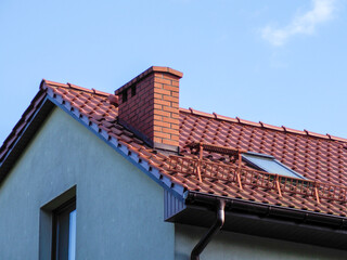 A low-angle shot of a red tile roof and a white chimney against a bright blue sky.