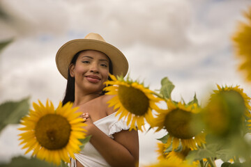 Portrait of a beautiful young Latina brunette woman wearing a white top and hat, hugging and loving...