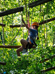 A person in a helmet and harness sitting on a wooden obstacle high in a ropes course, resting before continuing the climb.