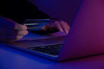 Hacker holding a credit card while accessing a system with a laptop. Concept of cybercrime, online fraud, identity theft, hacking, and digital security risk