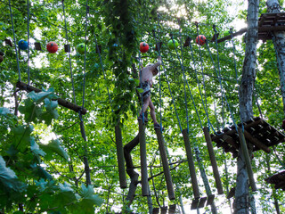 Fototapeta premium A person in a helmet and harness carefully traversing a suspended obstacle made of wooden bars and ropes in a ropes course.