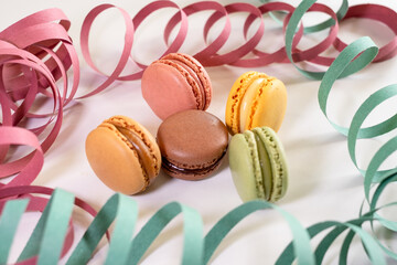 French macarons in pastel shades of green, yellow, pink, and brown. Festive streamers in the background add a celebratory and cheerful mood, perfect for party, dessert, or holiday themes