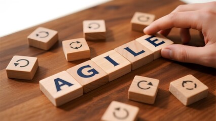 Hand arranging wooden blocks spelling 'AGILE' on a wooden surface