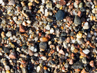 A detailed close-up shot of a textured, dry surface of colorful pebbles and sand, highlighting the variety of shapes and colors.