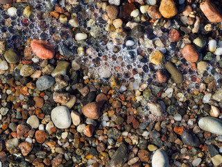 A detailed close-up of a textured beach surface with wet, colorful pebbles, sand, and small patches...
