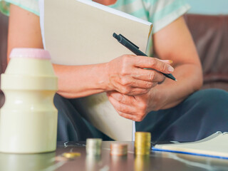 Close-up senior woman hand taking notes income and expenses. Retirement planning to save money. Saving earnings in a piggy bank. Lifestyle people concept retired life, financial or account economy 
