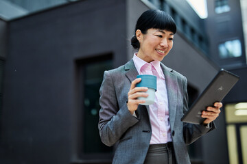 Portrait of a young asian japanese businesswoman woman using a tablet computer and holding a cup of...