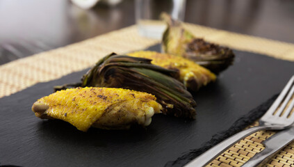 cooked fried chicken wings and halves artichokes on black stone plate