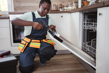 Technician repairing dishwasher in modern kitchen