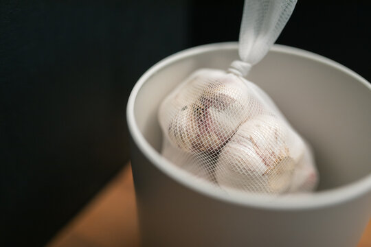 Close up of garlic bulbs in mesh bag inside white canister with black background