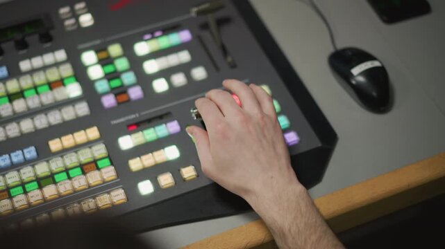 Close-up of hand operating control panel with colored buttons in TV production control room. Focused operator using video switcher in live broadcast or media production studio environment