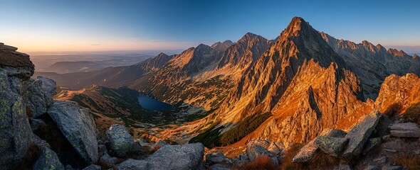 Golden light bathes a rugged mountain range at dawn, revealing a serene alpine lake nestled amongst the peaks and valleys, evoking a sense of vastness and tranquility.