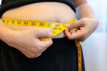 A woman checking her waist with measuring tape, symbolizing health, fitness, dieting, body fat, and weight loss goals