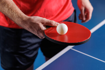 Table tennis serve preparation with red paddle and ball over blue table closeup