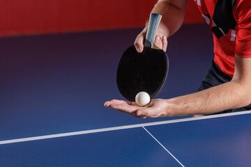 Table tennis serve preparation with black paddle and ball over blue table closeup