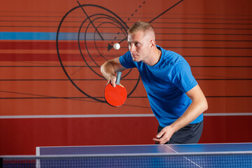 Focused table tennis player serving with red paddle during indoor match