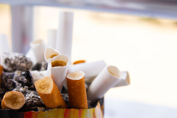 A detailed, close-up shot shows a cluster of burnt-out cigarettes and butts with their filters exposed, filling a rusty or old ashtray