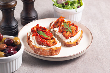 Two bruschettas with dried tomatoes, ricotta cheese and rucola on ciabatta bread. 