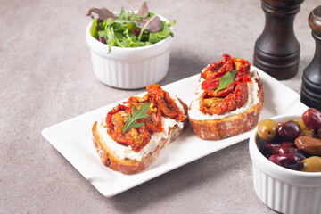 Two bruschettas with dried tomatoes, ricotta cheese and rucola on ciabatta bread. 