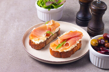 Two bruschettas with prosciutto, ricotta cheese and rucola on ciabatta bread. Olive and spices  decorated.