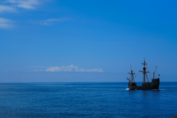 Vintage sailing ship replica cruising on calm blue ocean under clear sky, historical wooden galleon on tranquil sea with copy space.