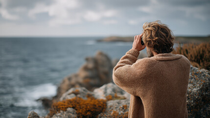 Man Observing Ocean Landscape with Binoculars, Peaceful Relaxation on Rocky Coastline