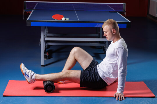 Male athlete uses a foam roller after table tennis practice on an indoor court for recovery mobility and injury prevention